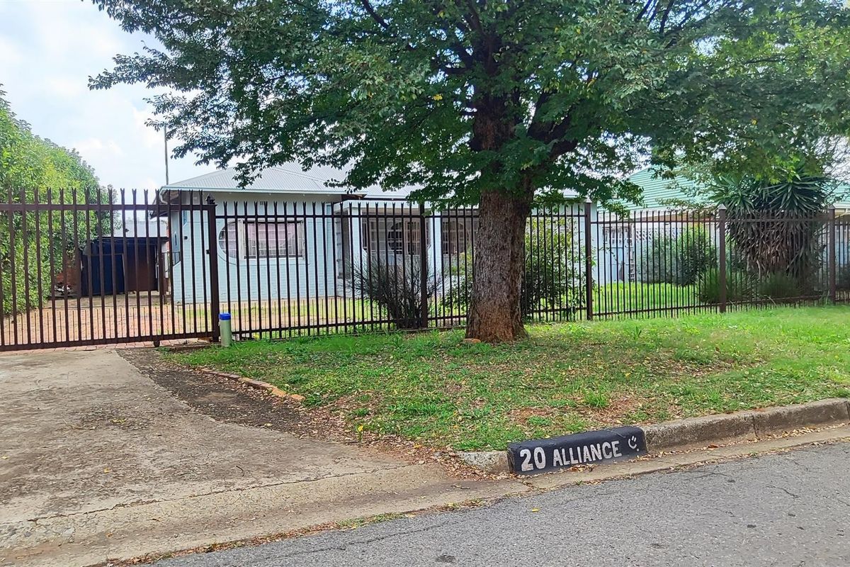 Front view of a residential property featuring a metal security fence, sliding gate, concrete driveway, and a brick facade with a tiled roof.