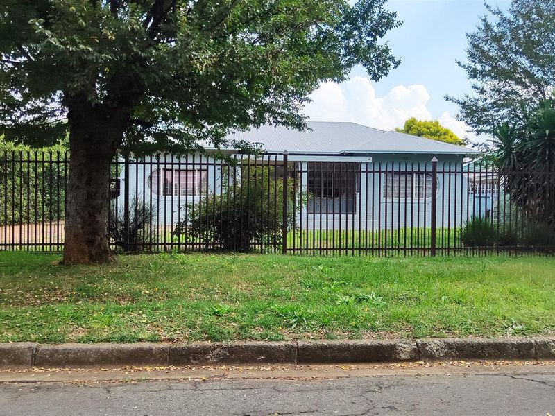 Front view of a residential house featuring a metal security fence, corrugated roof, and security bars on the windows.