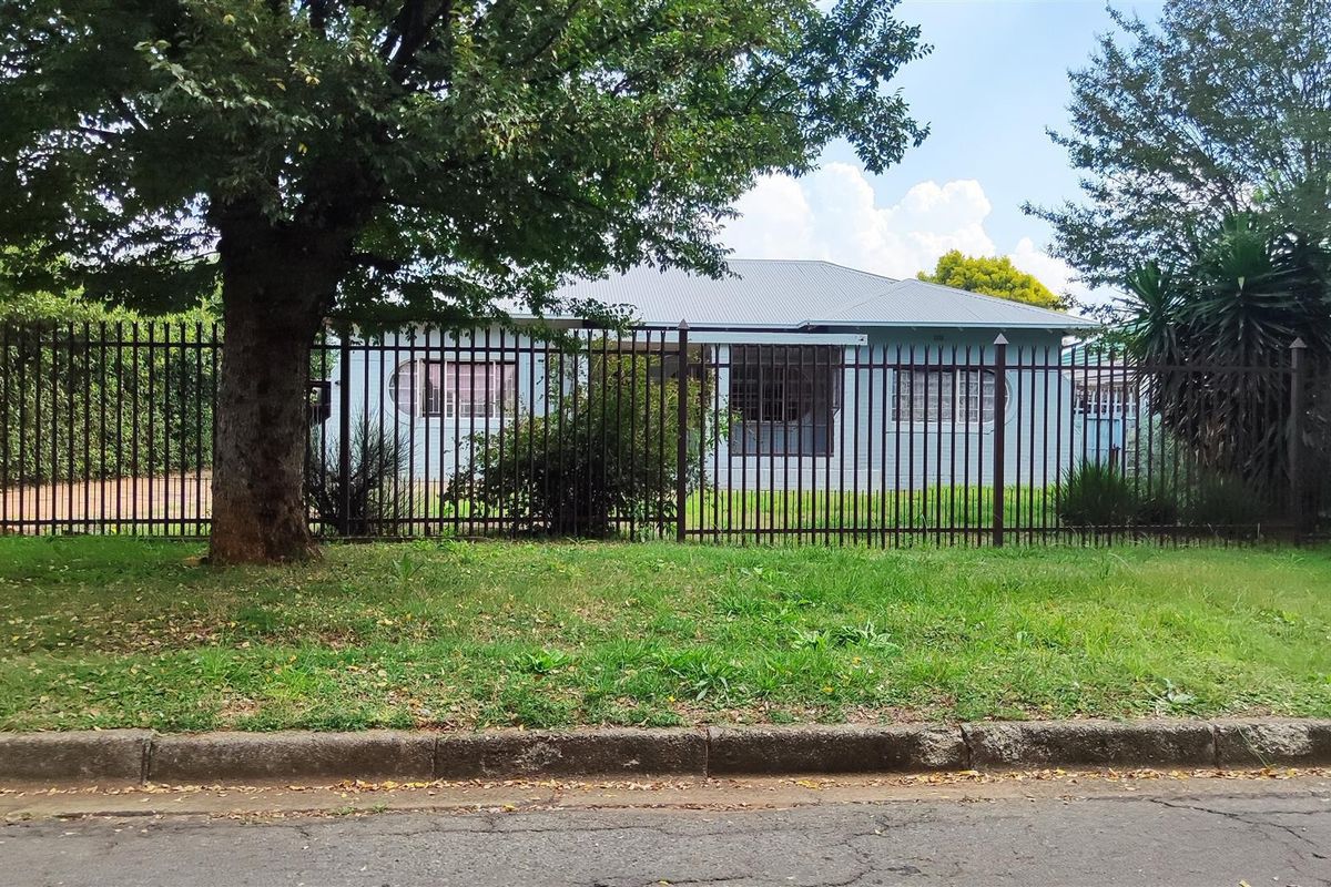 Front view of a residential house featuring a metal security fence, corrugated roof, and security bars on the windows.