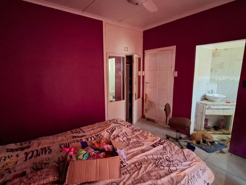 Bedroom featuring built-in cupboards and an en-suite bathroom, requiring cosmetic updates and repairs to wall finishes and door frames.