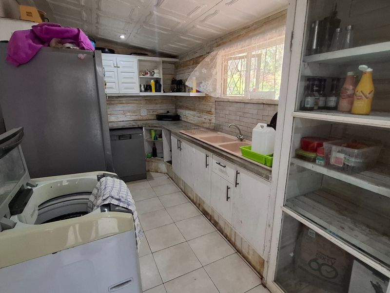 A functional kitchen featuring tiled flooring, a double basin sink, and built-in cabinetry with ample storage space, requiring cosmetic updates.