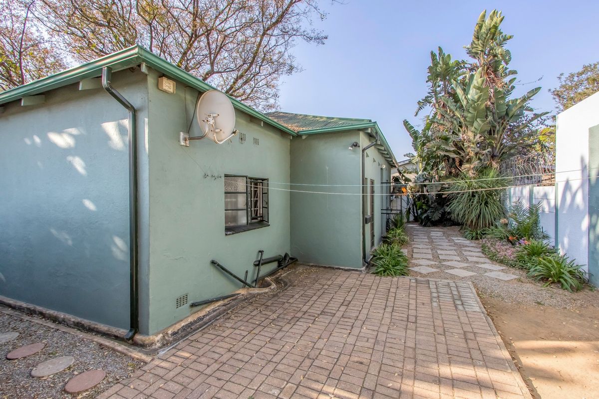 Rear exterior view of the property featuring a paved patio area, established garden, and external plumbing fixtures along the side wall.