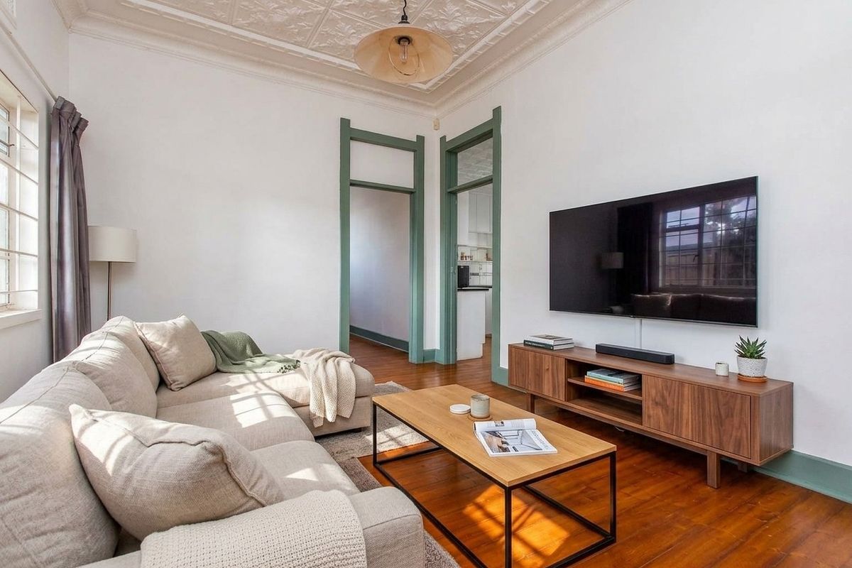 A bright living room featuring original pressed metal ceilings, polished timber flooring, and character-filled green-painted architraves.