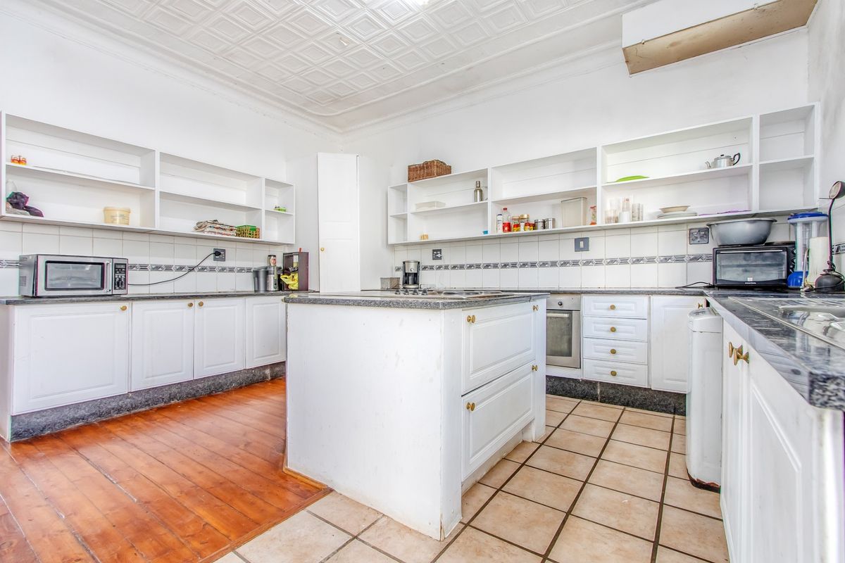 Spacious kitchen featuring a central island, built-in oven, hob, open shelving, and a mix of timber and tiled flooring under a classic pressed metal ceiling.
