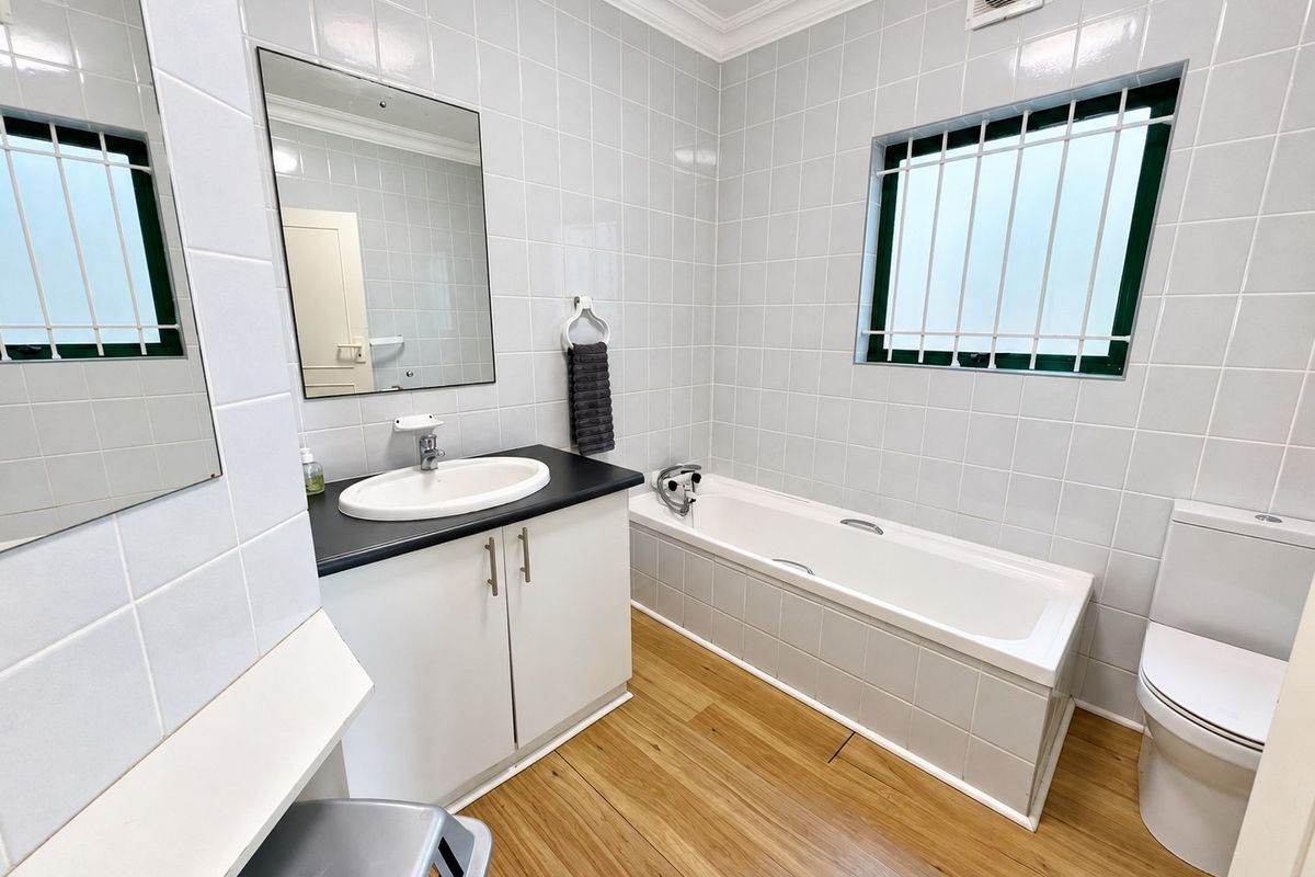 A clean, well-maintained bathroom featuring a vanity with basin, a bathtub, a toilet, and tiled walls with security bars on the window.