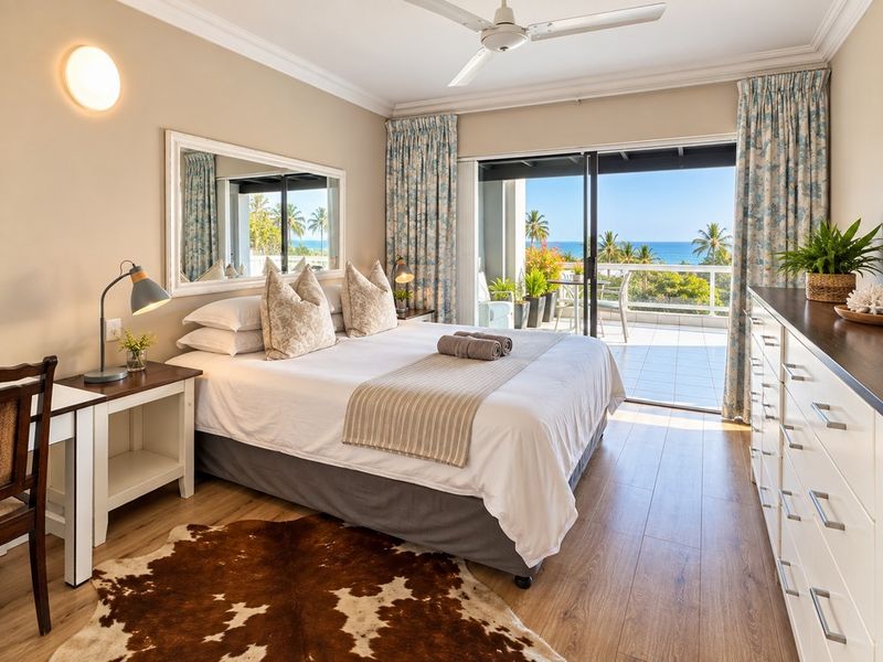A well-maintained bedroom featuring laminate flooring, crown molding, and a sliding glass door that opens onto a balcony with ocean views.