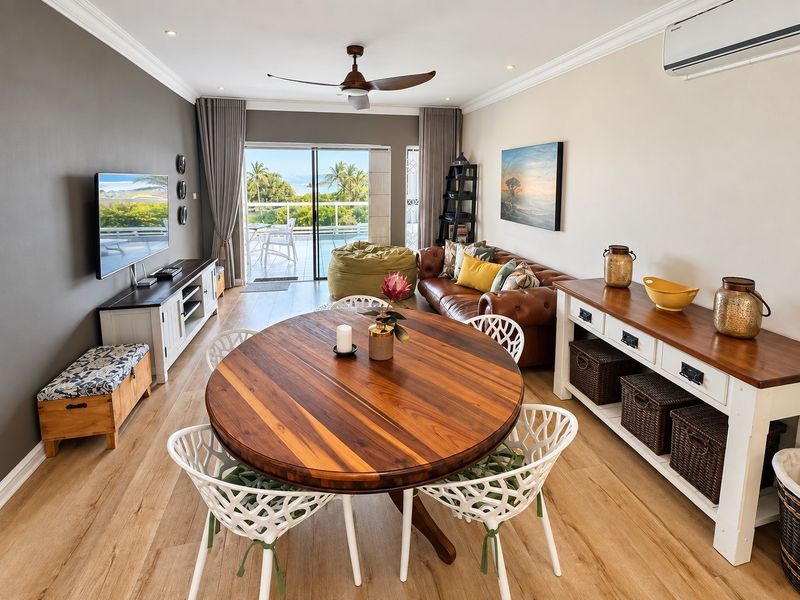 Spacious open-plan living and dining area featuring laminate flooring, crown molding, a ceiling fan, and sliding doors leading to a balcony with scenic views.