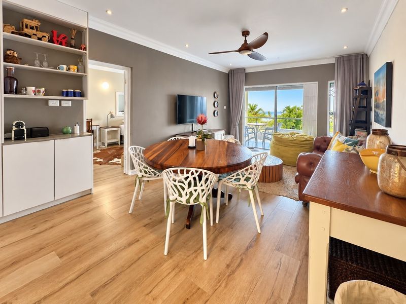Spacious open-plan living and dining area featuring modern laminate flooring, built-in shelving, and large sliding doors leading to a balcony with scenic views.