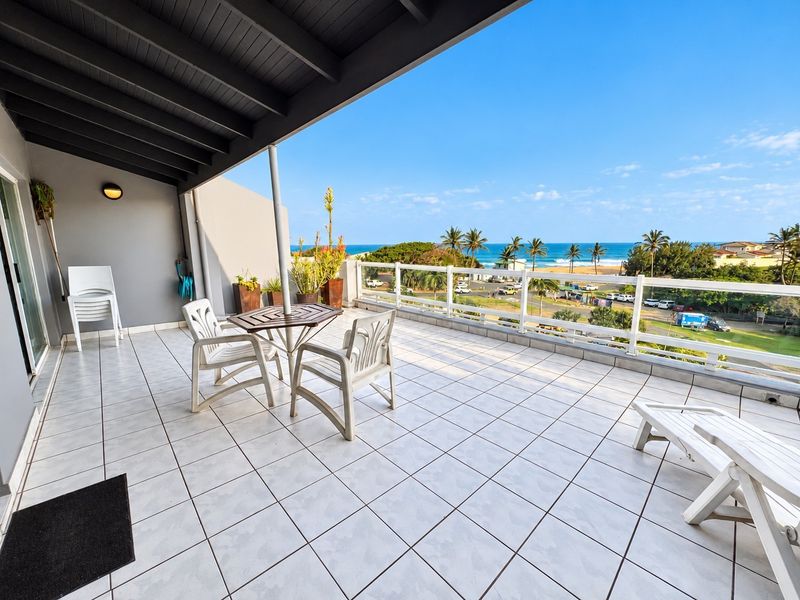 Spacious covered balcony featuring tiled flooring and a protective railing, offering expansive views of the coastline and ocean.