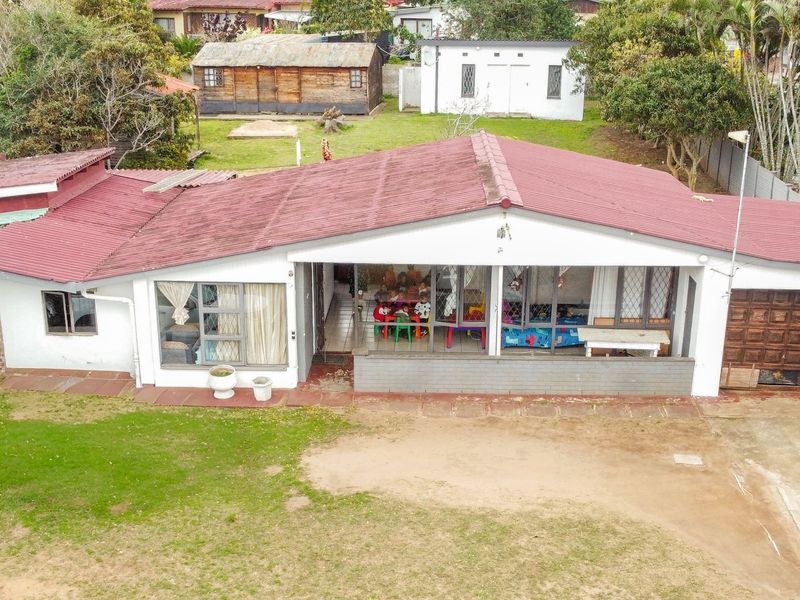 Aerial view of a single-story residential house featuring a corrugated metal roof, sliding glass doors, and an attached garage with a large garden area.