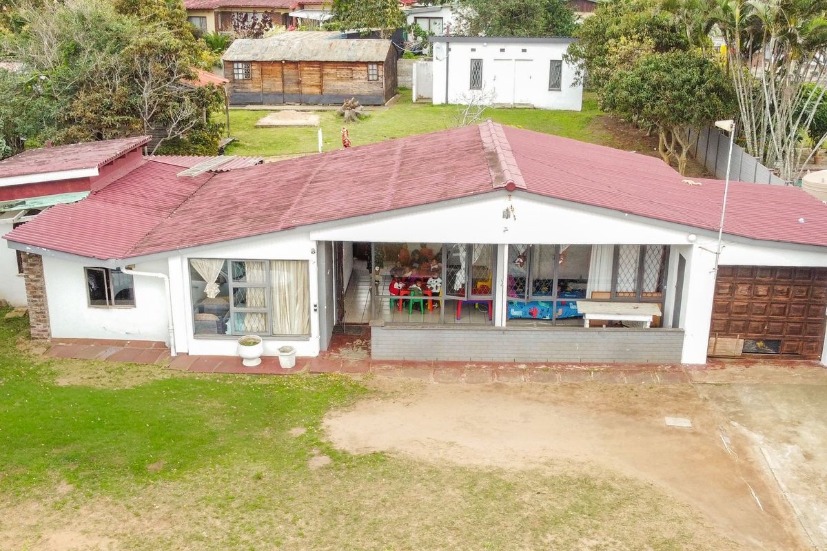 Aerial view of a single-story residential house featuring a corrugated metal roof, sliding glass doors, and an attached garage with a large garden area.