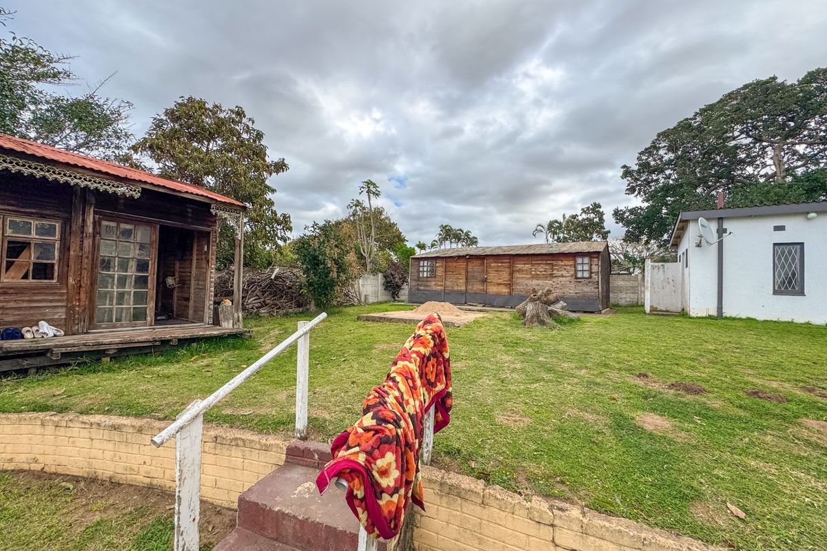Spacious rear garden area featuring a timber cabin, brick retaining wall with stairs, and additional outbuildings on the property grounds.