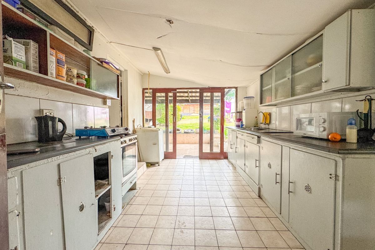 A dated kitchen featuring tiled flooring, built-in cabinetry, and direct access to the rear garden through glass sliding doors.