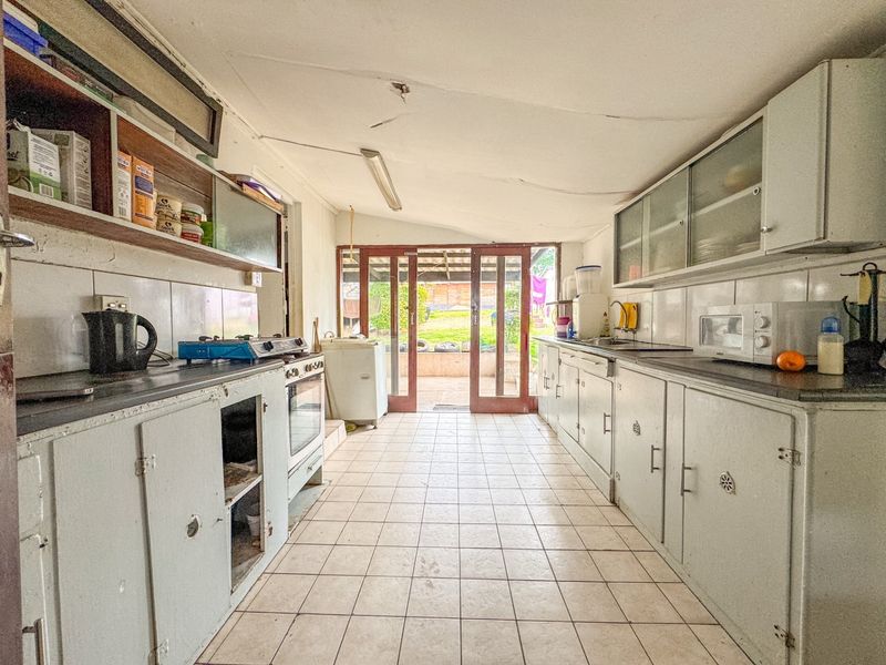 A dated kitchen featuring tiled flooring, built-in cabinetry, and direct access to the rear garden through glass sliding doors.