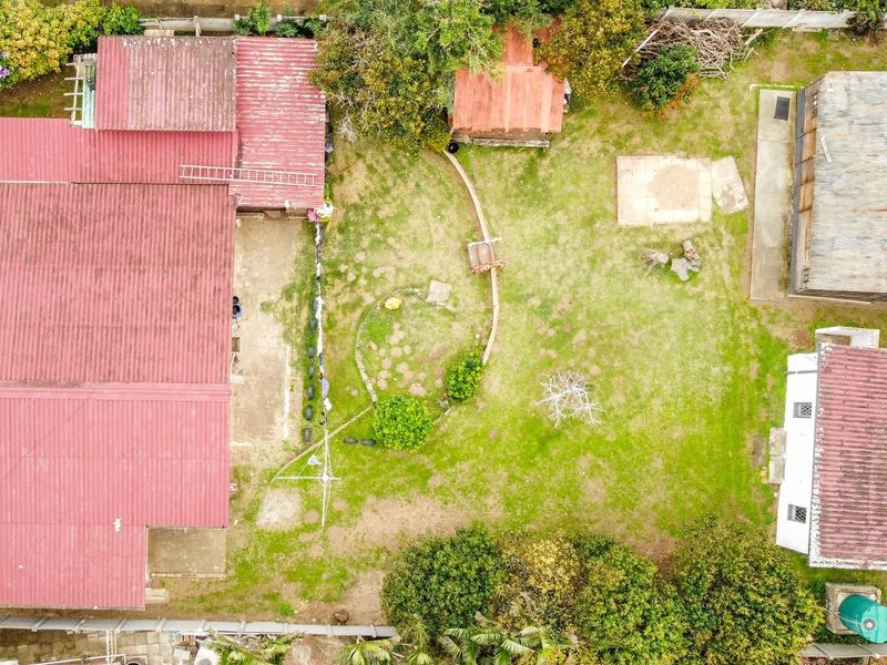 Aerial view of the property grounds featuring a main dwelling with a metal roof, a large garden area, and a detached outbuilding.