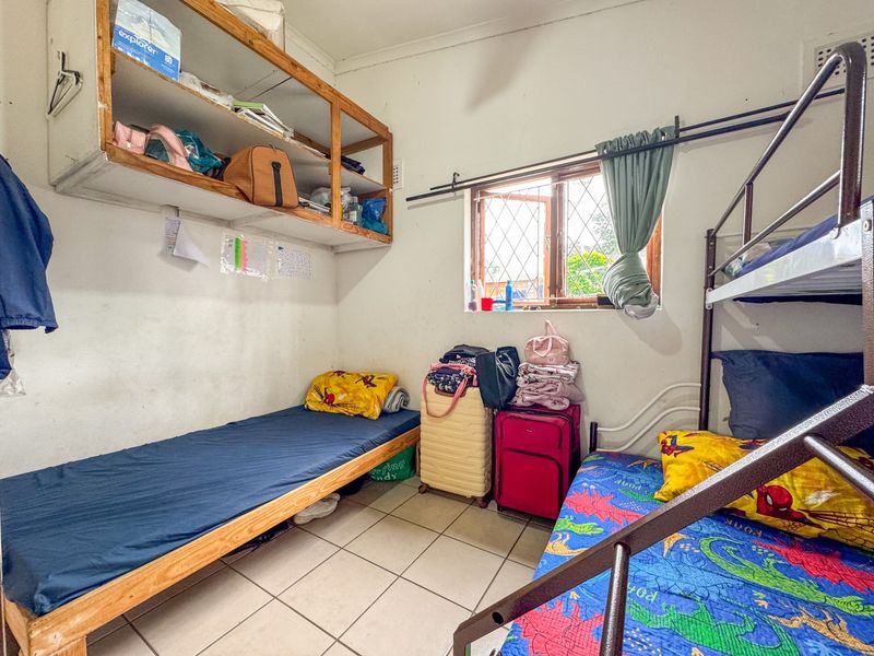 A functional bedroom featuring tiled flooring, built-in wall shelving, and a window with security bars, offering a practical layout for a compact living space.