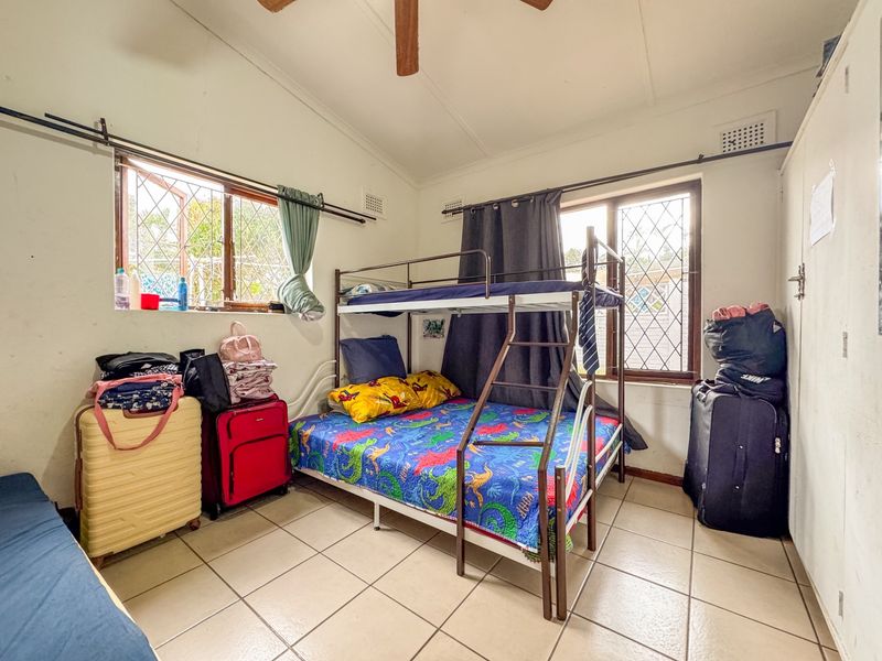 A bedroom featuring tiled flooring, a ceiling fan, and security bars on the windows, with built-in wardrobe storage.