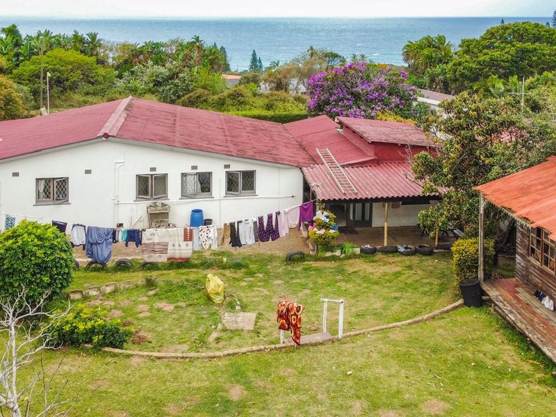 Aerial view of a residential property featuring a main house with a red roof, a separate timber outbuilding, and a spacious garden area.