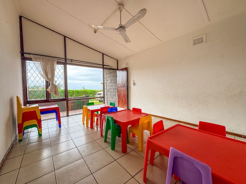 A spacious living area featuring tiled flooring, a ceiling fan, and large windows with security bars, offering direct access to the outdoor area.