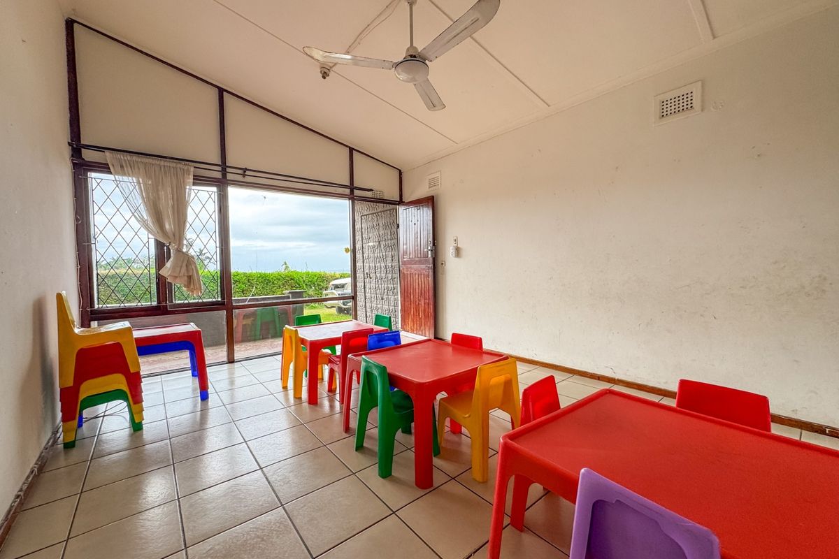 A spacious living area featuring tiled flooring, a ceiling fan, and large windows with security bars, offering direct access to the outdoor area.