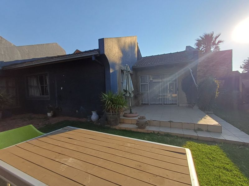 Rear view of the property featuring a tiled patio area, sliding glass doors, and a textured exterior finish with a small garden space.
