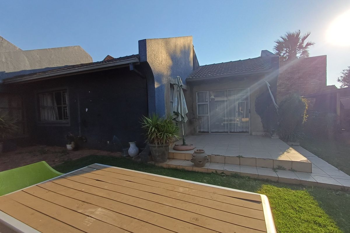 Rear view of the property featuring a tiled patio area, sliding glass doors, and a textured exterior finish with a small garden space.