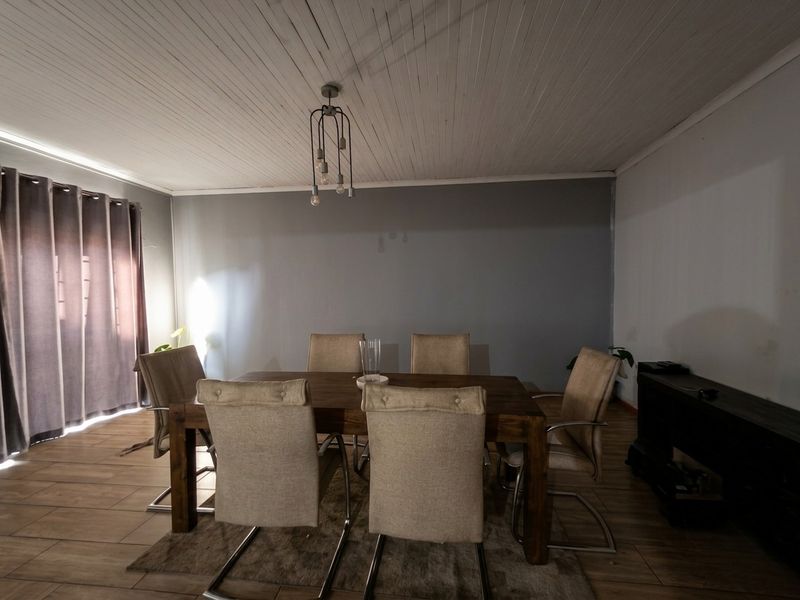 A dining room featuring timber-look tile flooring, a white tongue and groove ceiling, and a modern pendant light fixture.