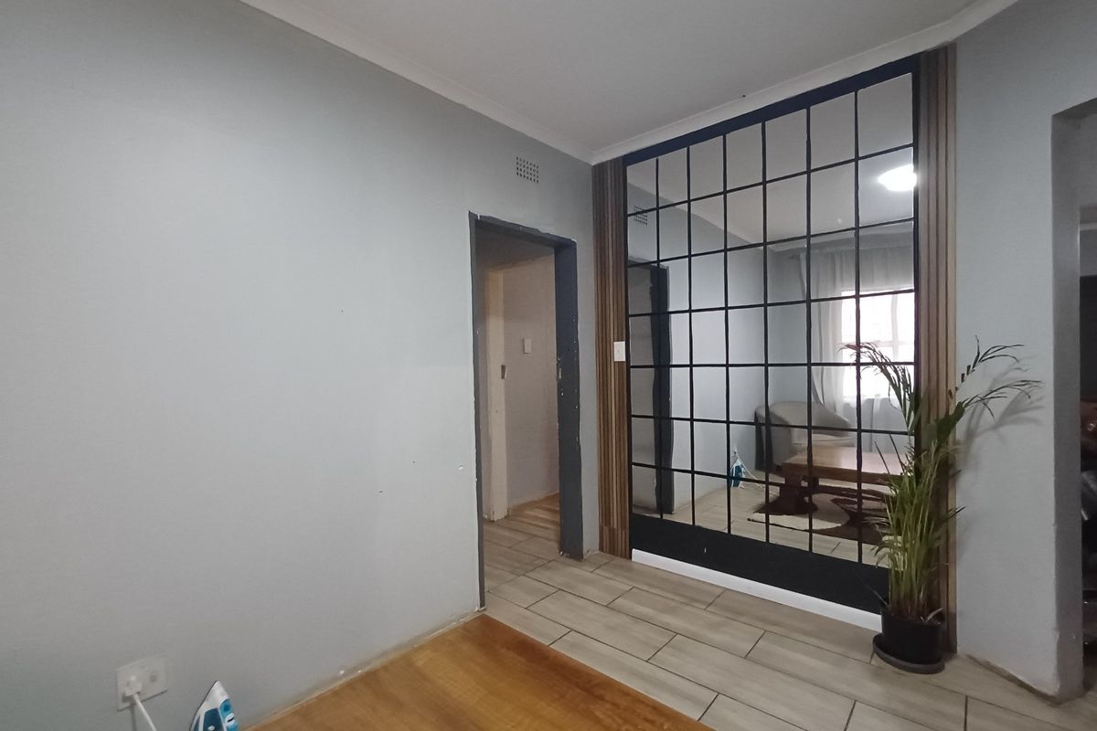 Living area featuring tiled flooring, a decorative grid-pattern mirror wall, and timber-look paneling, providing a contemporary aesthetic with potential for further finishing touches.