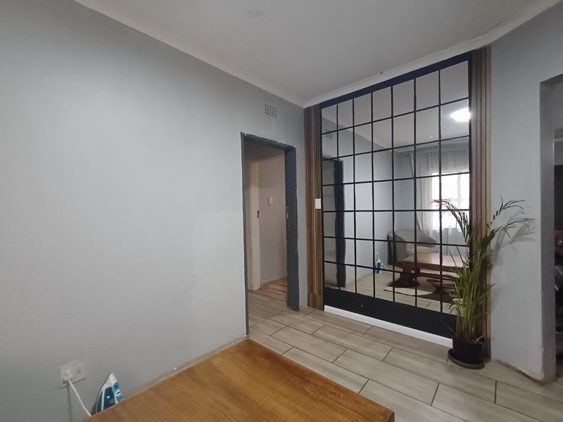 Living area featuring tiled flooring, a decorative grid-pattern mirror wall, and timber-look paneling, providing a contemporary aesthetic with potential for further finishing touches.