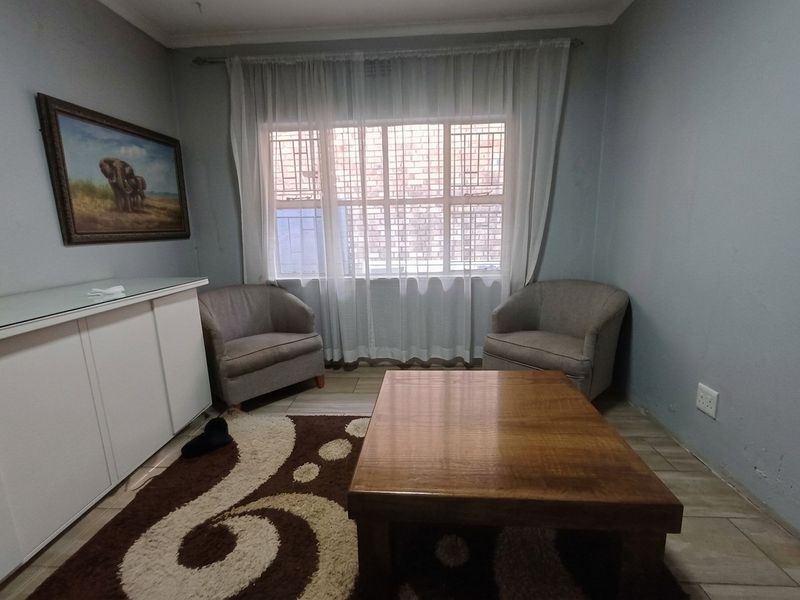 A cozy living room featuring tiled flooring, a large window with security bars, and neutral wall finishes.