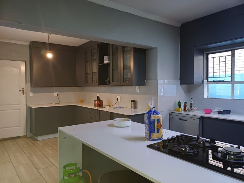 Modern kitchen featuring dark cabinetry, stone countertops, a central island with a gas hob, and tiled flooring.