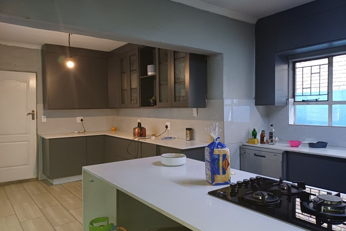 Modern kitchen featuring dark cabinetry, stone countertops, a central island with a gas hob, and tiled flooring.