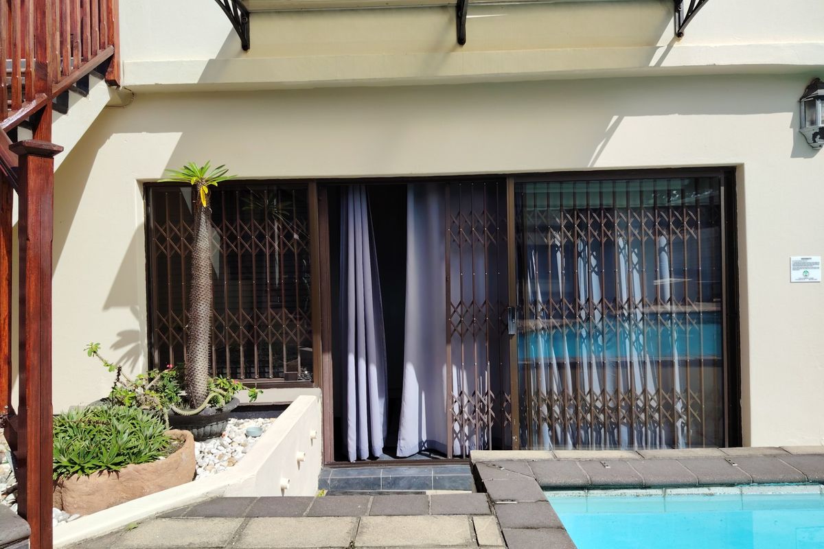Rear exterior view featuring a swimming pool, paved patio area, and sliding glass doors with security gates.