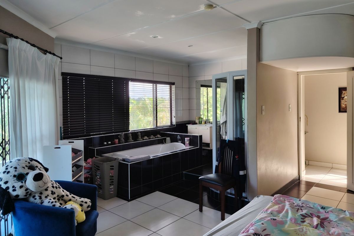 Spacious bedroom featuring an integrated en-suite bathtub area with tiled finishes, large windows with blinds, and neutral floor tiles.