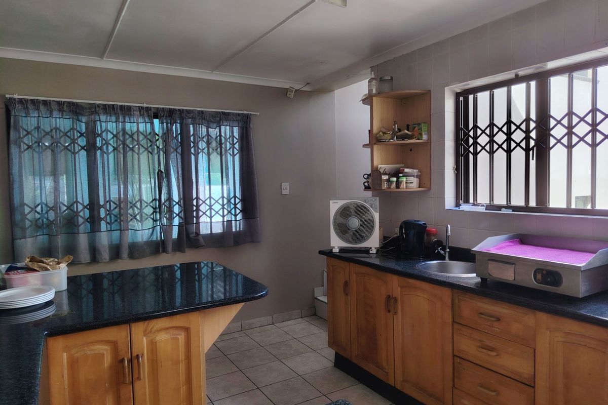 A functional kitchen featuring wooden cabinetry, granite countertops, tiled backsplash, and security gates on the windows, offering a practical layout for daily use.