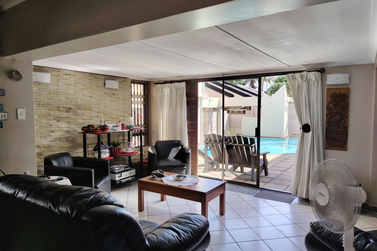 Spacious living room featuring a stone accent wall, ceramic tile flooring, and large sliding glass doors providing direct access to the outdoor pool area.