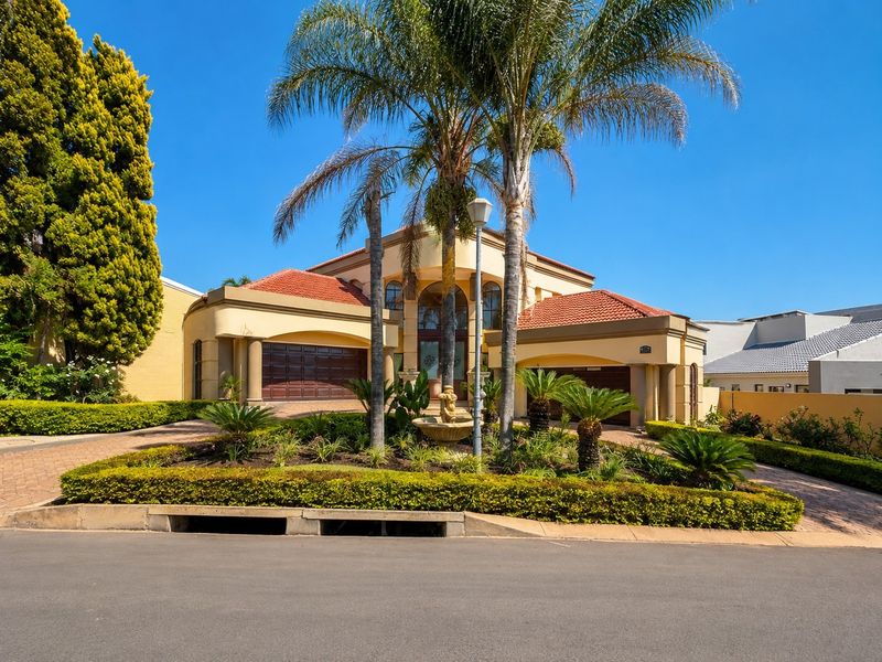 A well-maintained double-story residence featuring a paved driveway, double garage, and a beautifully landscaped front garden with mature palm trees and a central fountain.