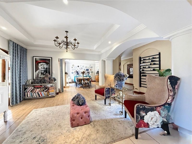 Spacious open-plan living area featuring elegant tray ceilings, hardwood flooring, and a distinctive arched transition between the lounge and dining spaces.