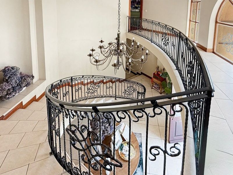 Grand entrance foyer featuring a sweeping curved staircase with ornate wrought iron balustrades and a classic chandelier, finished with neutral floor tiles.