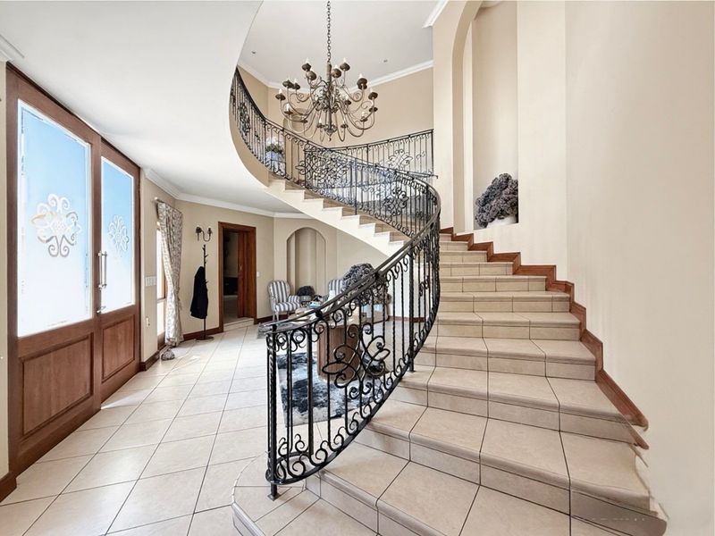 Grand entrance foyer featuring a sweeping tiled staircase with ornate wrought iron balustrade, arched wall niches, and a decorative chandelier.
