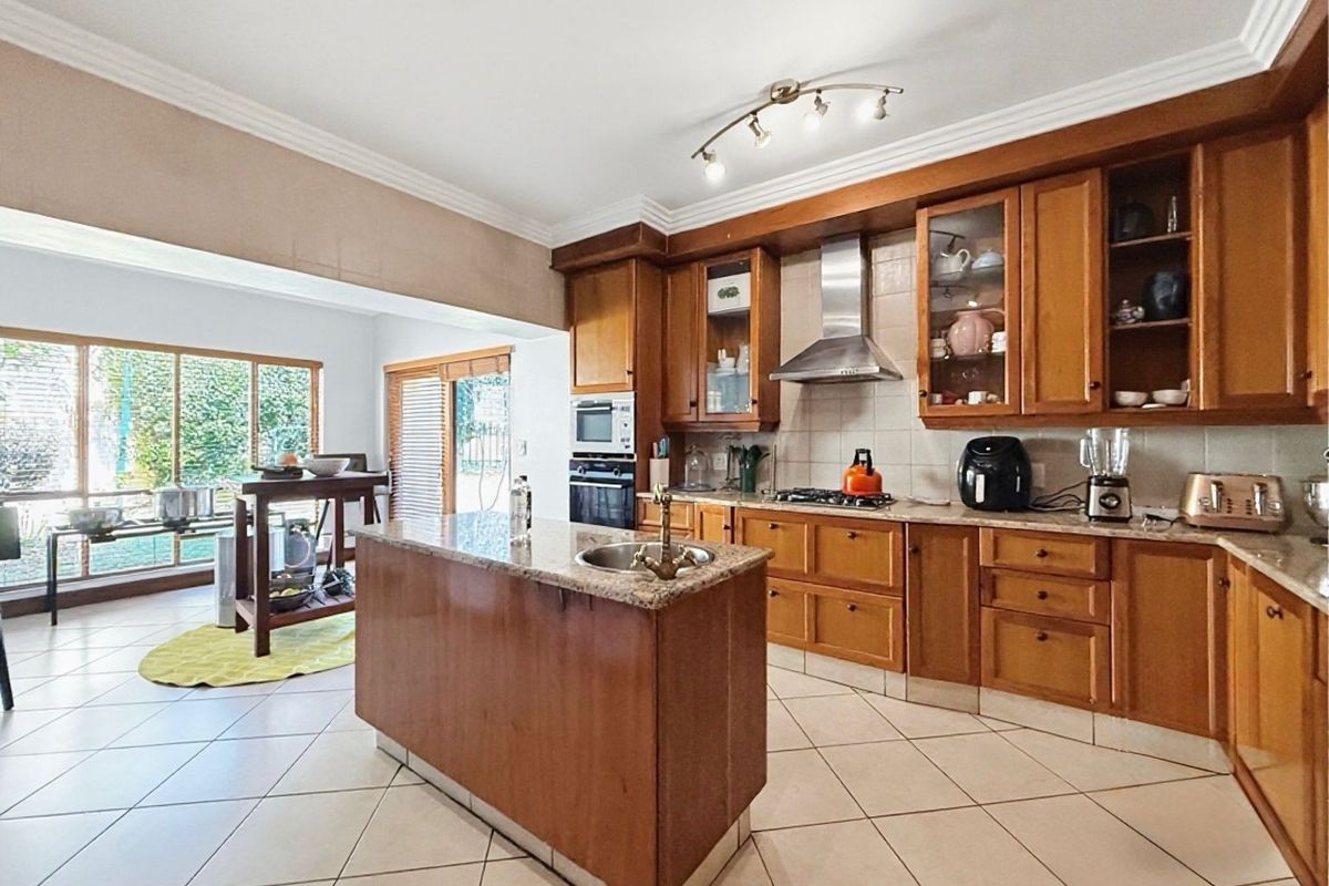 Spacious kitchen featuring wooden cabinetry, granite countertops, a central island with a prep sink, and integrated appliances, flowing into an adjacent living area.