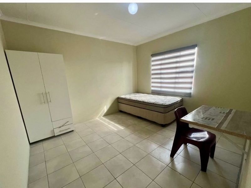 A simple bedroom featuring tiled flooring and roller blinds, providing a functional and neutral living space.