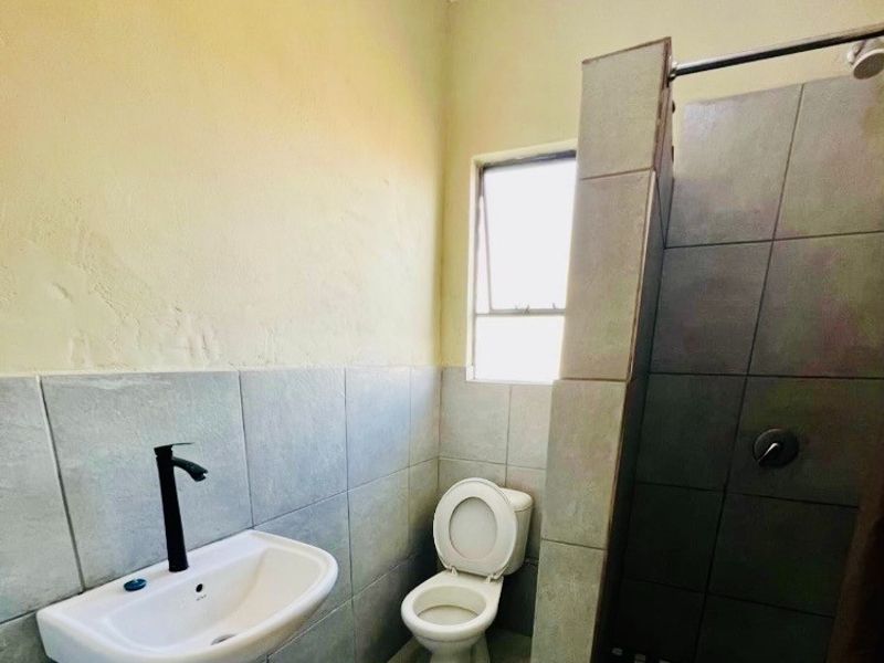 A functional bathroom featuring a basin with modern black tapware, a standard toilet, and a tiled shower enclosure with a window for natural light.