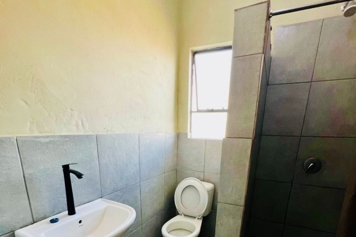 A functional bathroom featuring a basin with modern black tapware, a standard toilet, and a tiled shower enclosure with a window for natural light.