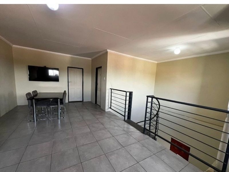 An open-plan living area featuring tiled flooring and a metal staircase railing, providing a functional space with neutral wall finishes.