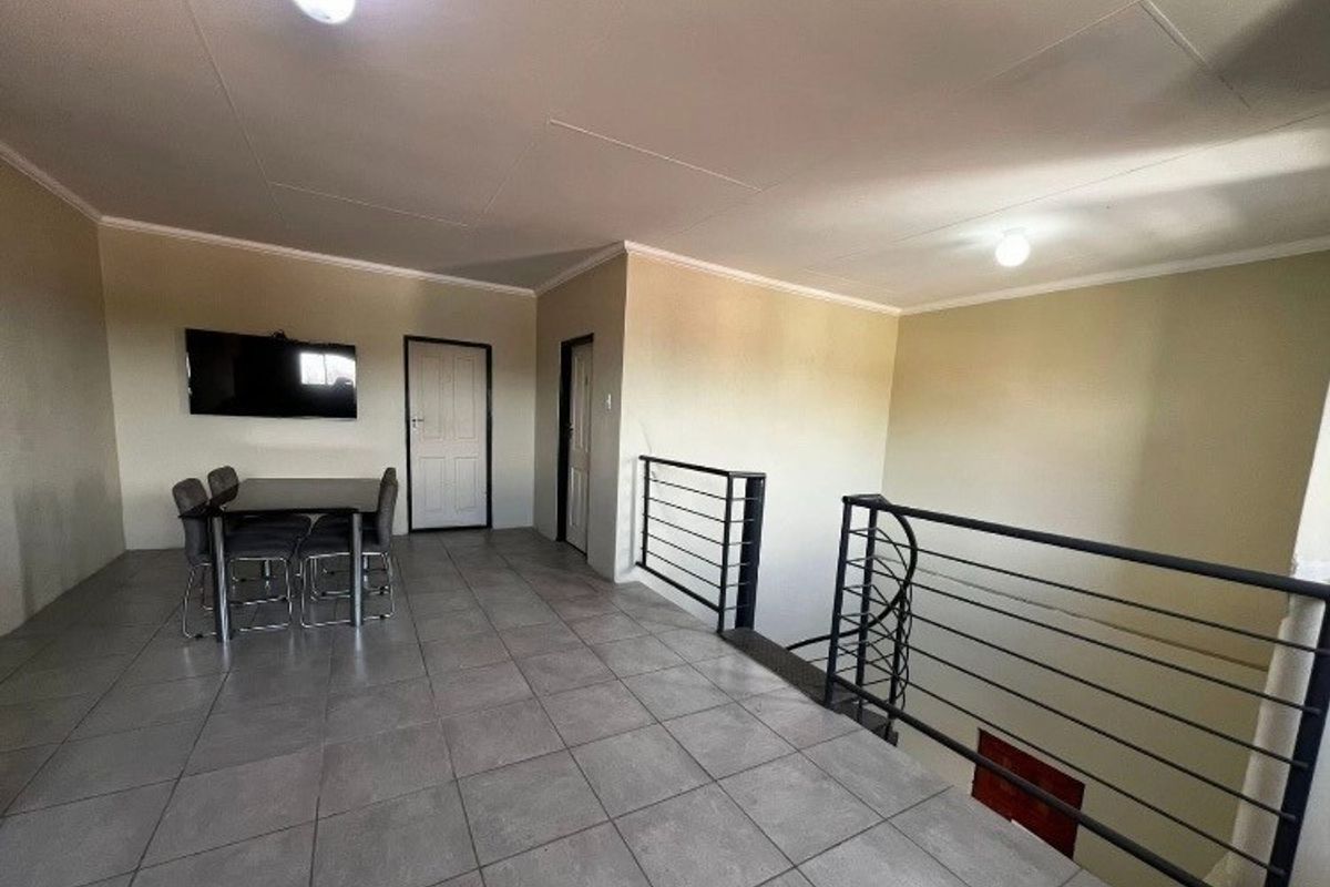 An open-plan living area featuring tiled flooring and a metal staircase railing, providing a functional space with neutral wall finishes.