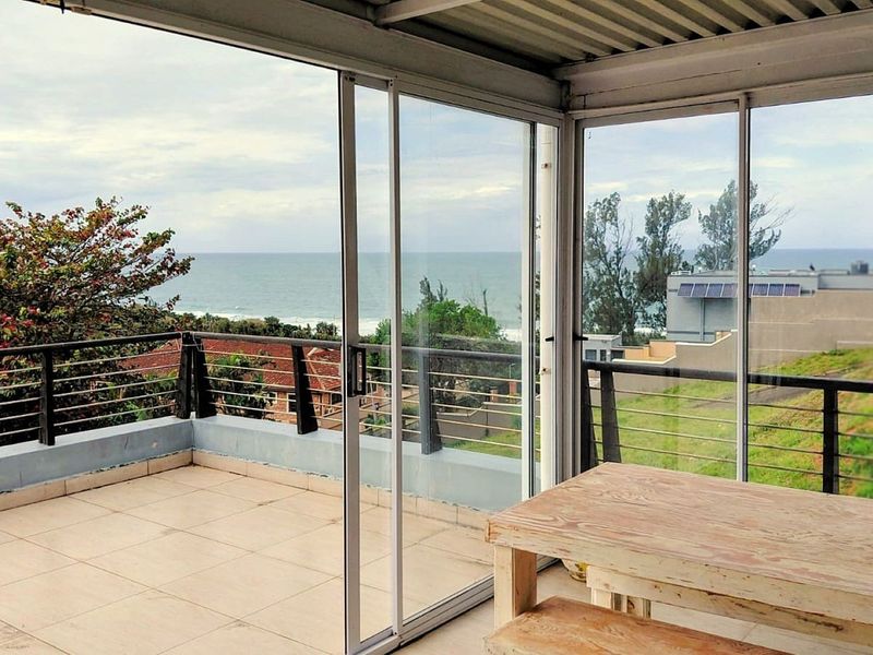 Spacious covered balcony featuring tiled flooring, sliding glass doors, and panoramic ocean views, offering a versatile outdoor living space.