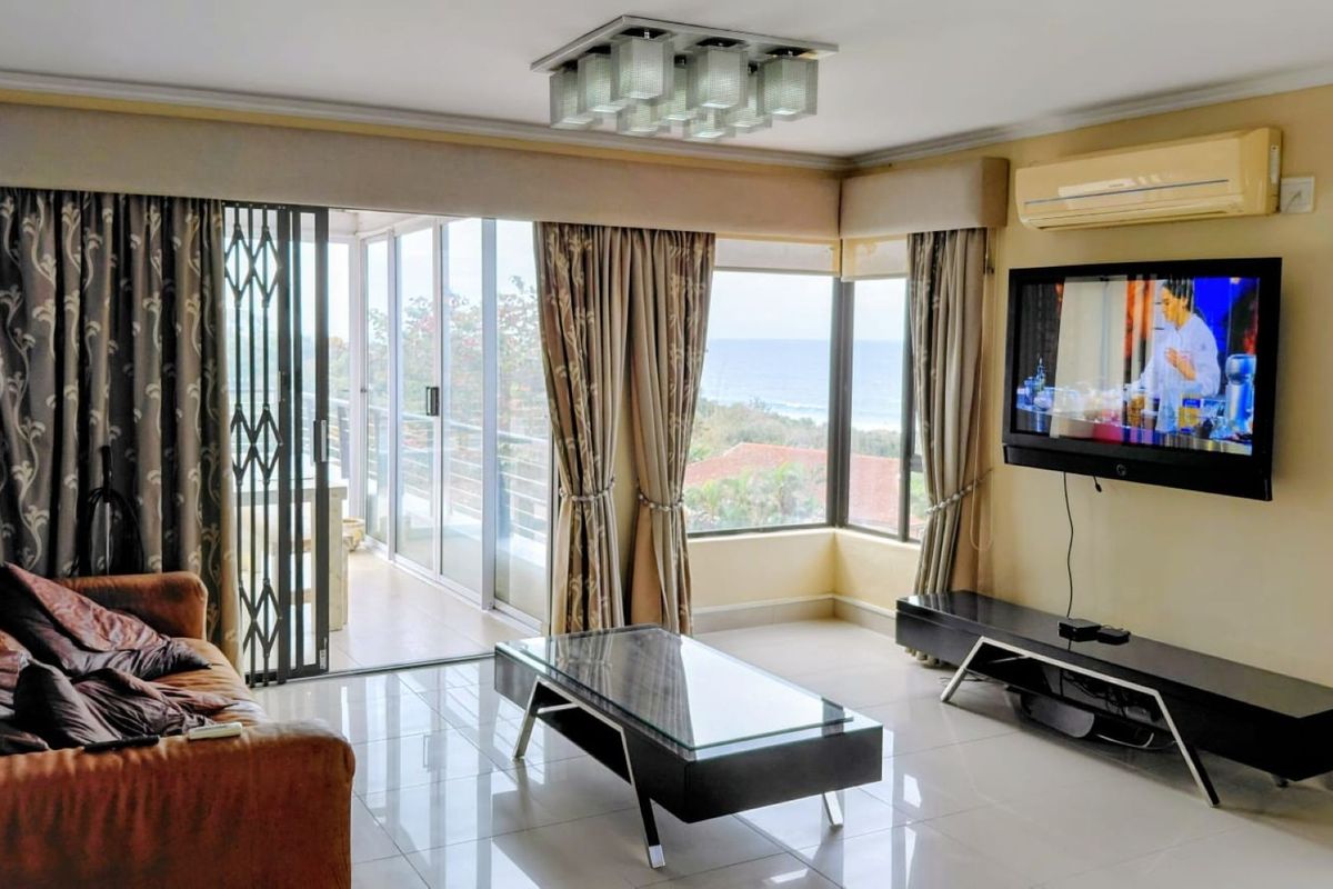 Spacious living room featuring tiled floors, a split-system air conditioner, and large sliding glass doors opening to a balcony with ocean views.