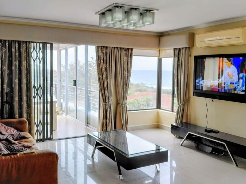 Spacious living room featuring tiled floors, a split-system air conditioner, and large sliding glass doors opening to a balcony with ocean views.