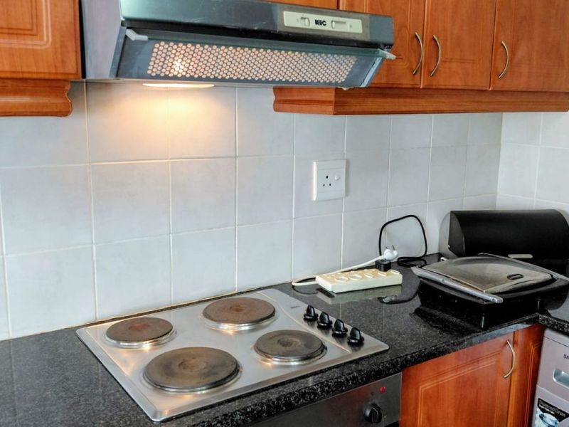 A functional kitchen area featuring dark granite countertops, tiled backsplash, wooden cabinetry, and a built-in electric hob with an overhead extractor fan.
